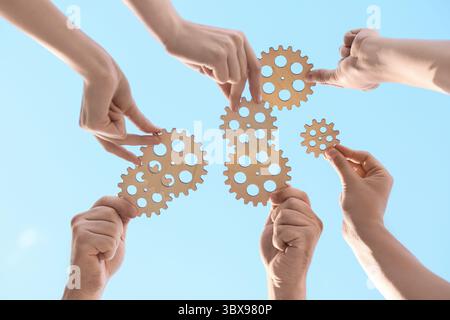 Many hands with wooden gears against sky, bottom view Stock Photo