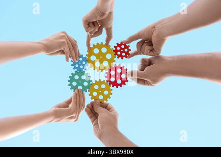 Many hands with colorful gears against sky, bottom view Stock Photo