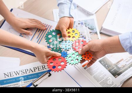 Hands of engineers with colorful gears at table in office, closeup Stock Photo