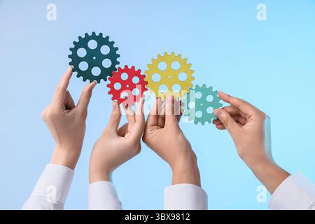 Female hands with colorful gears on light background Stock Photo