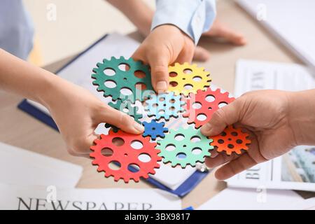 Hands of engineers with colorful gears at table in office, closeup Stock Photo