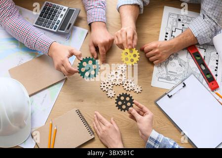 Hands of engineers with gears on table, top view Stock Photo