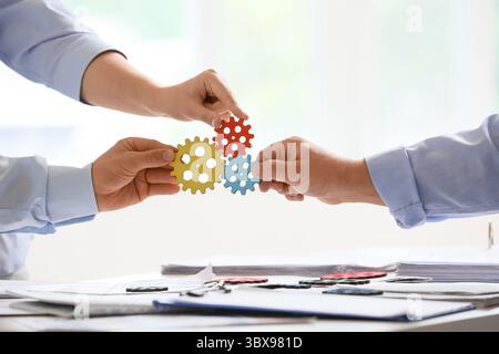 Hands of engineers with gears in office, closeup Stock Photo