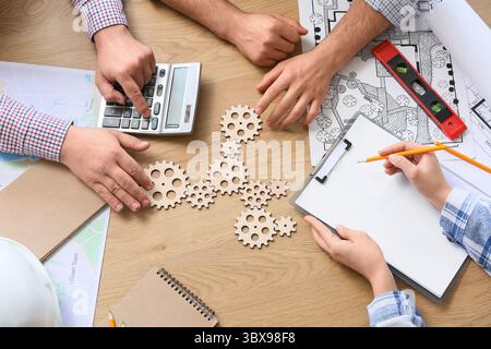 Hands of engineers with gears working on table, top view Stock Photo