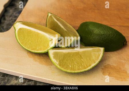 Close-up of sliced lime wedges on wooden cutting board Stock Photo