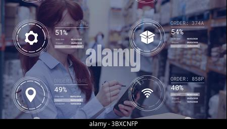 Holding tablet with stylus, female worker scanning inventory in warehouse aisle, with digital icons Stock Photo