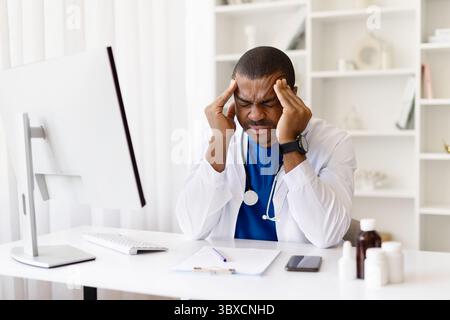 Stressed young African American doctor holding head in pain, suffering headache Stock Photo