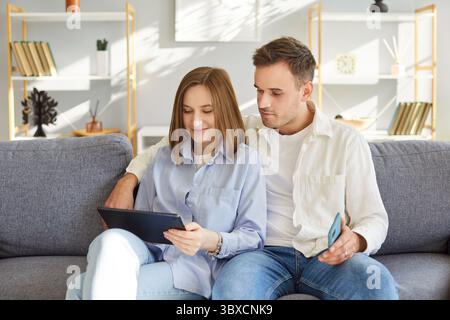 Happy spouses, smiling couple in love using tablet computer together at home, talking on video call Stock Photo
