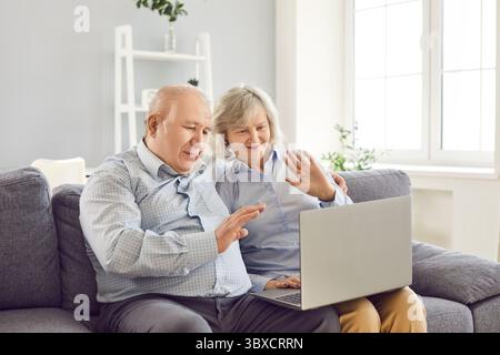 Elderly Couple Using Laptop for Video Call and Waving Greetings Stock Photo