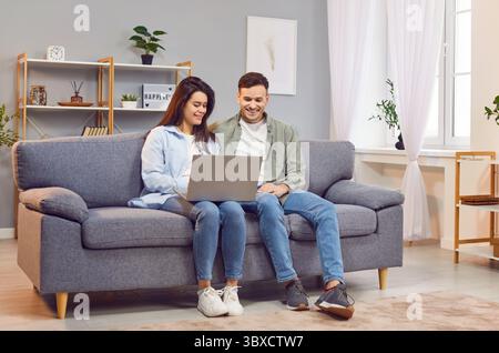 Happy couple at home, young woman and man sitting close in new modern living room, using laptop  Stock Photo