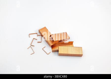 A scattering of copper-toned staple refills, some in strips and others loose, arranged on a clean white background. Stock Photo