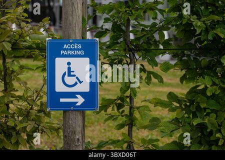 A blue sign among natural greenery indicating a parking space suitable for disabled access, marked with a white wheelchair symbol. Stock Photo