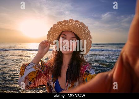 Smiling woman on beach at sunset wearing a straw hat Stock Photo