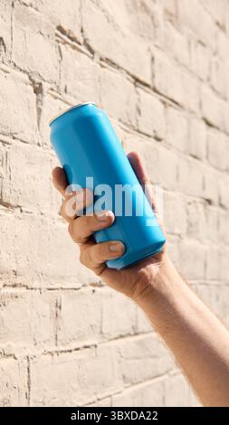 Hand holding cyan blue drink can near brick wall for branding mockup Stock Photo