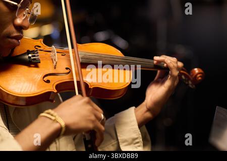 Black man playing violin with focused expression, close up on hands and instrument, adult musician performing on stage, wearing glasses, showcasing musical talent and concentration Stock Photo
