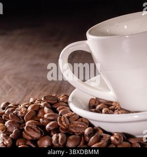 This close-up image features a pristine white porcelain coffee cup elegantly set among roasted coffee beans, highlighting the contrast between the cup Stock Photo