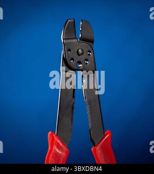 Professional electrical cable crimping pliers displayed on a vibrant blue gradient background, showcasing precision tools for electrical projects. Ide Stock Photo
