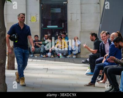 Blue-collar and white-collar workers share a lunch break in the City of London, UK ,  construction workers sit on steps while office staff relax on designated seating, capturing the diverse workforce that fuels the capital’s financial and commercial heart Stock Photo