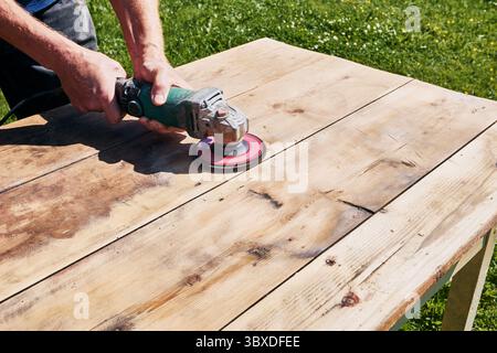 Sanding wooden surface with abrasive disc on angle grinder, power tool smoothing tabletop in precise close-up during woodworking process Stock Photo