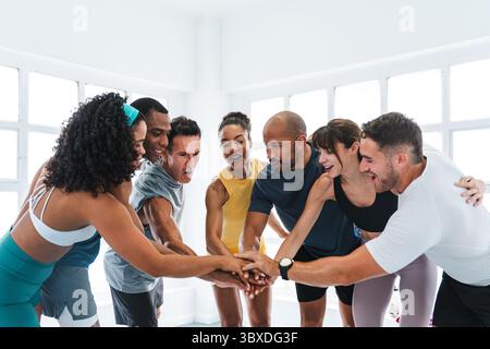 Multiethnic group of sportive people doing functional workout in training class gym cheerful multi-ethnic athletes in sportswear joining hands after a Stock Photo
