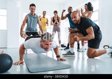 Multiethnic group of sportive people doing functional workout in training class gym motivated athletes supporting determined sportsman performing push Stock Photo