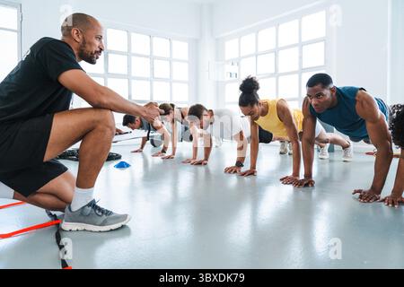 Multiethnic group of sportive people doing functional workout in training class gym diverse athletes performing push-ups on the gym floor while follow Stock Photo