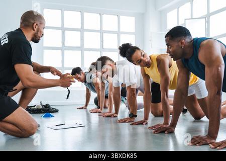 Multiethnic group of sportive people doing functional workout in training class gym group of determined athletes performing bear crawls under the guid Stock Photo