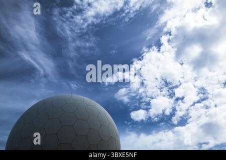 A modern radar spherical structure set against a vivid blue sky with clouds, evoking advanced technological innovations and futuristic design elements Stock Photo