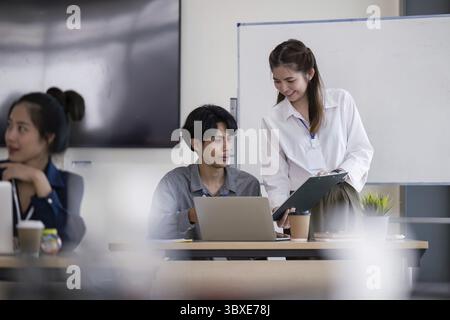 A business team engaged in analyzing data and discussing strategy in a modern office environment, featuring laptops and a whiteboard Stock Photo