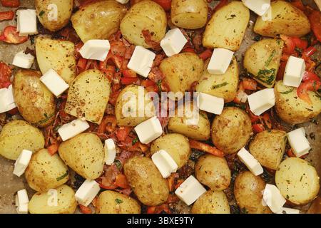 Colorful roasted potatoes and red peppers are arranged on a baking tray, topped with cubes of feta cheese. The dish has been seasoned with herbs and i Stock Photo