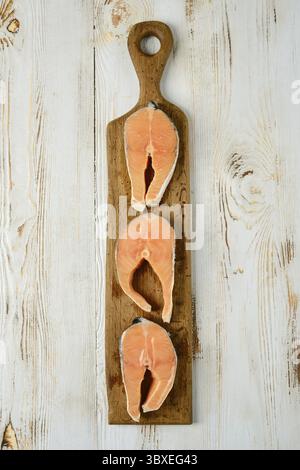 Three slices of fresh salmon steaks cross cut are arranged on a rustic wooden cutting board Stock Photo