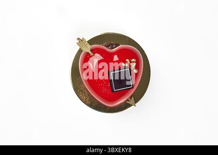Vibrant red heart-shaped strawberry mousse cake with glossy icing, chocolate and gold arrow, perfect for celebrations of love and affection on Valenti Stock Photo