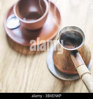 Hot coffee with steam in oriental Turkish style served in cezve, a small long-handled pot with a pouring lip and cup on a wooden table Stock Photo