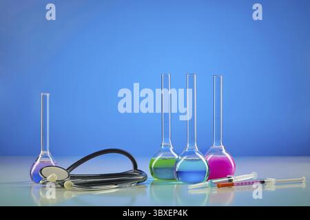 Four medical flasks with colorful chemical reagents. Testing kit, syringe and phonendoscope, blue background. Laboratory research Coronavirus. Worldwi Stock Photo