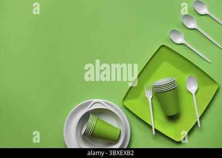 Colorful plastic disposable tableware, such as plates and bowls, four spoons, fork and folded cups on green background with copy space. The concept of Stock Photo