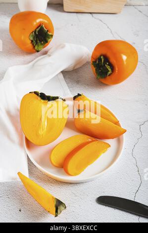Food, Plate with pieces of sweet tasty persimmon on white background vertical view Stock Photo
