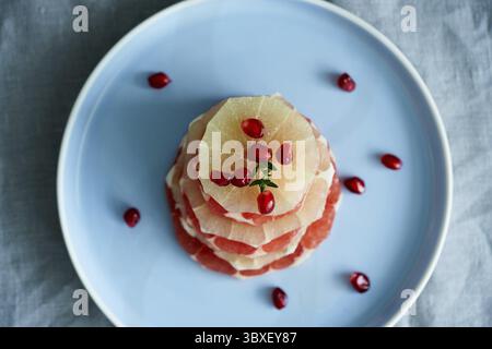 Top view stack of sliced round slices of red and white grapefruit sprinkled with pomegranate seeds on blue plate. Bright mix of citrus fruits Stock Photo