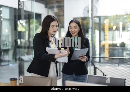 Two business partners review documents and a tablet, showcasing teamwork and strategic planning in a contemporary office Stock Photo