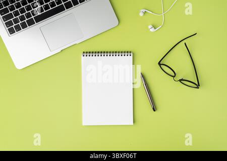 Blank empty space on white spiral notepad for text, cropped laptop keyboard, earphones, black glasses, fountain pen on light green background, copy sp Stock Photo
