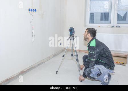 Man makes repairs in new apartment. Builder levels walls using laser level. Stock Photo