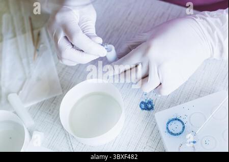 Food, Female hands in gloves pour sparkles into a mold for making a pendant from epoxy resin Stock Photo