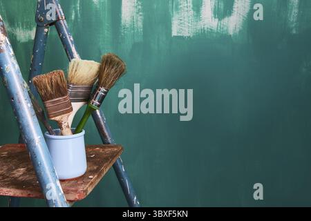 Background for text about repair and wall painting in the apartment. Tassels and stepladder on a green background. Copy space Stock Photo
