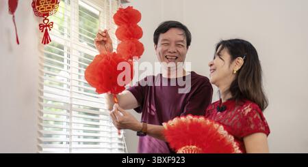 Elderly chinese couple celebrating new year with traditional decorations at home joyful atmosphere heartwarming moment Stock Photo