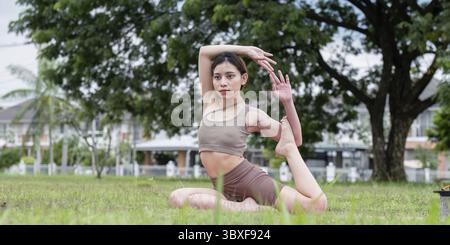 A young woman practicing an advanced yoga pose outdoors in a park, showcasing flexibility and concentration Stock Photo