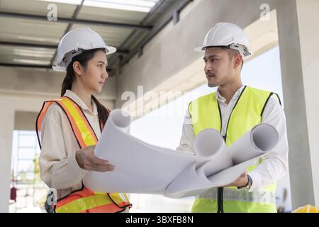 Two engineers reviewing construction blueprints on site, focusing on design and coordination for the project Stock Photo