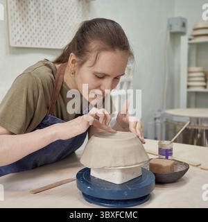 Concentrated young woman ceramist working on clay ware with satisfaction as recreation in creative art studio Stock Photo