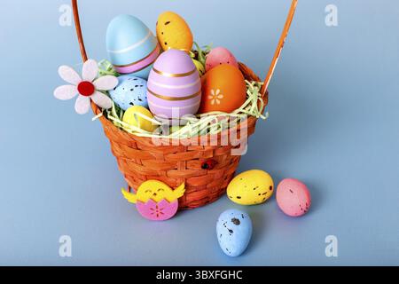 Close up of wicker basket filled with decorative multi colored easters eggs on a light blue background Stock Photo