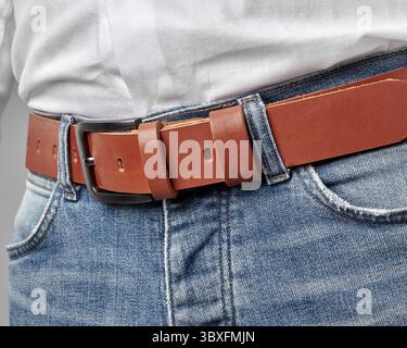 Closeup of terracotta leather belt with custom DAD embossing on loop complementing casual look of man dressed in jeans and white shirt. Concept of qua Stock Photo