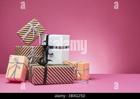 Different sizes, colorful, striped and plain, brown, rose and white paper gift boxes tied up with multicolored ribbons and bows on a pink surface and Stock Photo