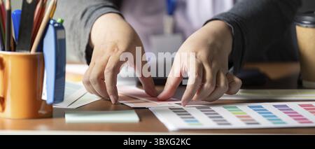 Close-up of a designer's hands meticulously arranging color swatches and palettes on a workspace, emphasizing the importance of color selection in gra Stock Photo